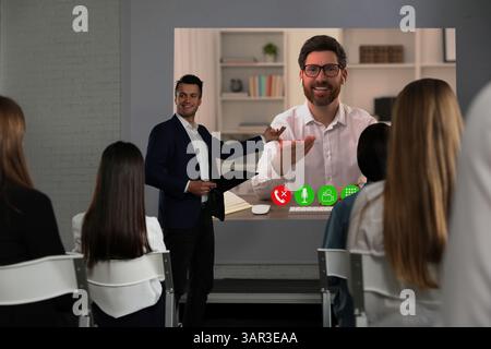 Redner, der über Online-Videochat an der Vorlesung teilnimmt. Publikum und Trainer im Konferenzraum mit Projektionsleinwand Stockfoto