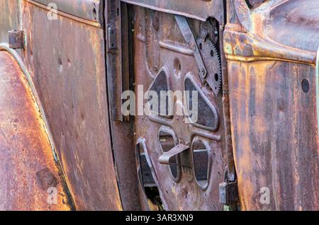 Nahaufnahme einer verrosteten antiken Autotür mit freiliegenden Zahnrädern und Metallarbeiten, oxidierten Texturen und Patina bei weichem Tageslicht. Stockfoto