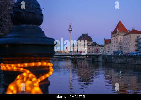 Berlins berühmter Fernsehturm und Bode-Museum, der zur blauen Stunde über die Spree mit warmen Lichtern und klarem Abendhimmel zu sehen ist. Stockfoto