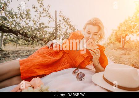 Frau, Picknick, Sommer: Die blonde Frau genießt Wassermelonen beim Picknicken im Freien auf einem sonnigen Sommerfeld. Stockfoto