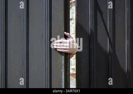 Man schließt oder öffnet von Hand ein dunkles Holztor. Nur Hand und Finger sind sichtbar. Nahaufnahme. Kopierbereich für Text. Stockfoto