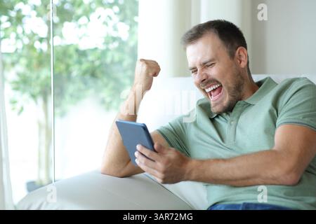 Ein aufgeregter Mann liest ein eBook, der zu Hause auf einer Couch sitzt Stockfoto
