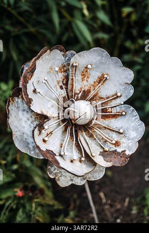 Nahaufnahme einer handgefertigten Metallblumenskulptur in einem Gartenbett. Das Kunstwerk erkundet rustikales Handwerk, von der Natur inspiriertes Design und aufgearbeitete Ästhetik Stockfoto
