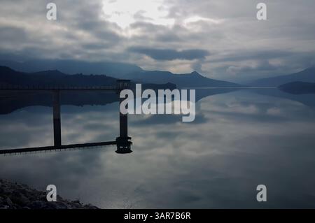 Ein ruhiger Morgen am See mit einem Einlassturm, reflektierenden Wolken und Bergen im ruhigen Wasser Stockfoto