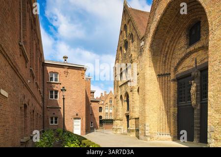 Schmaler Durchgang zwischen hohen mittelalterlichen Backsteinbauten des Sint-Janshospitaal in Brügge, Belgien, der an einem kunstvollen bogenförmigen Eingang vorbeiführt. Stockfoto