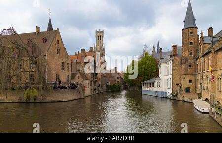 Der berühmte Rozenhoedkaai-Kanal in Brügge, Belgien, mit dem Glockenturm, historischen Giebelbauten und einer Trauerweide. Bedeckter Himmel. Stockfoto