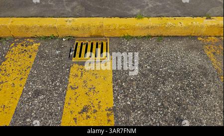 Gelb lackierte Bordsteinkante und Abflussabdeckung auf Asphaltstraße mit gelben Parkplätzen Stockfoto