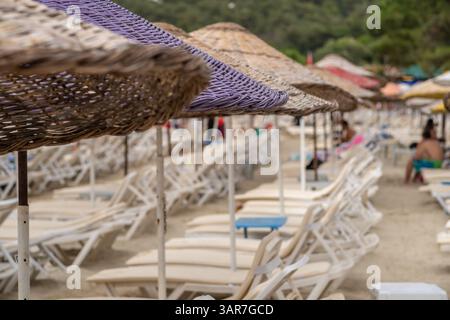 Besucher entspannen sich unter bunten Sonnenschirmen an einem Sandstrand auf Prince Islands, während sie das sonnige Wetter und den wunderschönen Blick auf die Küste genießen. Stockfoto