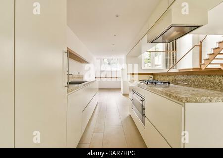 Eine geräumige und helle, moderne Küche mit eleganten Schränken, Granitarbeitsplatten und stilvollen Armaturen, die sowohl für Funktionalität als auch für Ästhetik konzipiert sind. Stockfoto