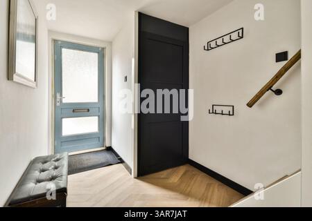 Ein eleganter und moderner Eingangsflur mit stilvoller blauer Tür, minimalistischer Einrichtung und schicker schwarzer Bank sowie attraktiven Wandhaken. Stockfoto