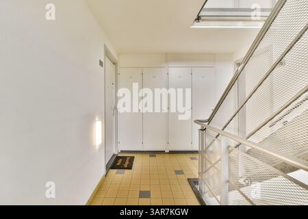 Ein eleganter Innenkorridor mit modernen Designelementen, darunter eine Treppe und Ablagefächer an den Wänden, beleuchtet durch Tageslicht. Stockfoto