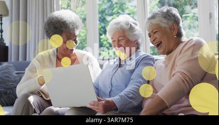 Bild von glücklichen älteren, verschiedenen weiblichen Freunden, die ein Notebook über Lichtflecken verwenden Stockfoto