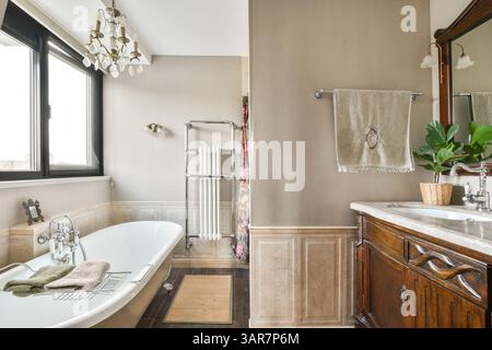 Ein geräumiges und stilvolles Badezimmer mit freistehender Badewanne, Holzwaschtisch und großen Fenstern, das Funktionalität mit ästhetischem Charme verbindet. Stockfoto