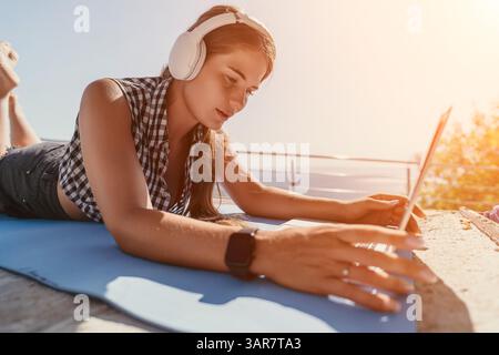 Frau im Kopfhörer mit Laptop an einem sonnigen Tag Stockfoto
