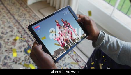 Bild eines Goldkonfetti, das über einen birassischen Mann fällt und Fußball auf einem Tablet beobachtet Stockfoto