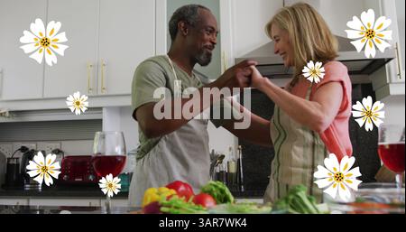 Bild von weißen Blumen über Seniorenpaaren, die in der Küche tanzen Stockfoto