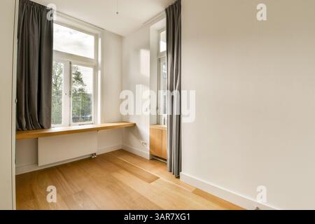 Helles und luftiges Zimmer mit elegantem Fensterdesign, weichen Vorhängen und Holzfußboden schaffen einen ruhigen und modernen Wohnbereich. Stockfoto
