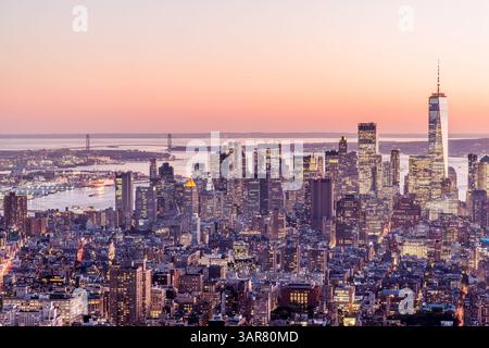Atemberaubender Blick auf den Sonnenuntergang über die Innenstadt von Manhattan mit leuchtenden Wolkenkratzern und warmen Lichtern der Stadt, die das Ambiente der goldenen Stunde widerspiegeln Stockfoto
