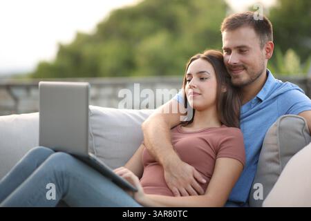 Ein Paar, das auf einer Couch auf einer Terrasse sitzt und den Laptop überprüft Stockfoto