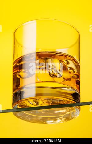 Ein klassisches Whiskyglas gefüllt mit goldenem Bernsteinwhiskey, gelber Hintergrund Stockfoto