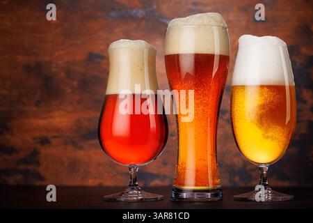 Eine Auswahl verschiedener Biergläser gefüllt mit verschiedenen Biersorten, elegant auf einem rustikalen Holztisch vor hölzernem Hintergrund angeordnet Stockfoto
