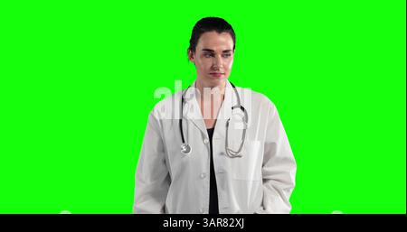 Junge Frau, die vor hellgrünem Hintergrund steht, weißen Laborkittel und Stethoskop trägt Stockfoto