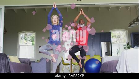 Bild von Herzsymbolen über Seniorenpaaren, die zu Hause Yoga üben Stockfoto