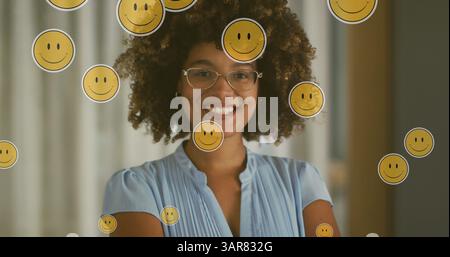 Bild von Emoji-Ikonen über glücklicher birassischer Frau Stockfoto