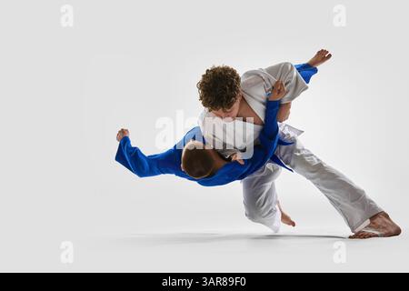 Dynamischer Mid-Air-Twist als Kämpfer in weiß bringt den Gegner mit starker Haltung ins Gleichgewicht, was Selbstvertrauen und Macht vor weißem Hintergrund veranschaulicht. Stockfoto