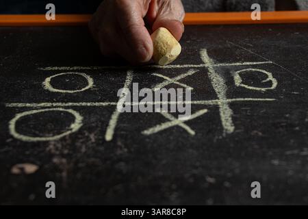 Kinderspiel Tic TAC Toe auf einer Schultafel gezeichnet und eine Frauenhand mit Kreide, Spiel Tic TAC Toe Stockfoto