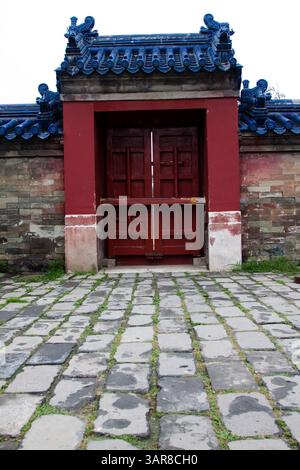 Peking, China, 14.07.2010. Eine rote Tür mit einem blauen Dach. Die Tür ist offen und der gemauerte Gang ist mit Moos bedeckt Stockfoto