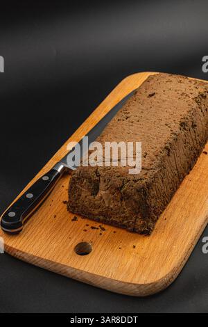Eine frisch zubereitete Hühnerleber-Pastete liegt auf einem hölzernen Schneidebrett, begleitet von einem scharfen Messer. Die reichhaltige Textur und die erdfarbene Farbe deuten auf das Delicio hin Stockfoto
