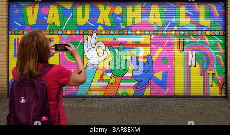 Frau, die ein Smartphone benutzt, um farbenfrohe Graffiti auf einem Ladenrollenladen in Vauxhall, Lambeth, London, England, Großbritannien zu fotografieren Stockfoto