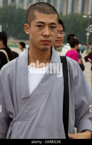 Peking, China, 14.07.2010. Ein Mann mit grauem Gewand und weißem Hemd steht vor einer Menschenmenge. Er hält eine schwarze Tasche in der Hand und sieht aus Stockfoto