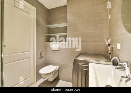 Ein elegantes und modernes Bad mit grauen Fliesenwänden, minimalistischen Regalen und modernen Armaturen schafft eine saubere und stilvolle Ästhetik. Stockfoto