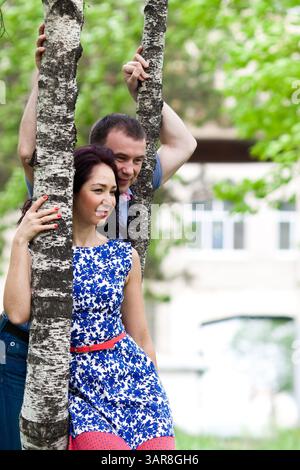 khabarovsk, russland, 06.07.2013. Ein Mann und eine Frau umarmen einen Baumstamm. Die Frau trägt ein blaues Kleid mit einem roten Gürtel Stockfoto