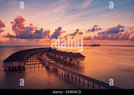 Blick aus der Vogelperspektive auf die atemberaubenden malediven Wasservillen während eines pulsierenden Sonnenuntergangs mit türkisfarbenem Wasser, tropischem Paradies und ruhiger Inselatmosphäre Stockfoto