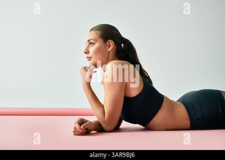 Die junge Frau in Activewear genießt einen Moment der Reflexion auf einer weichen rosa Matte, die Wellness anregt. Stockfoto