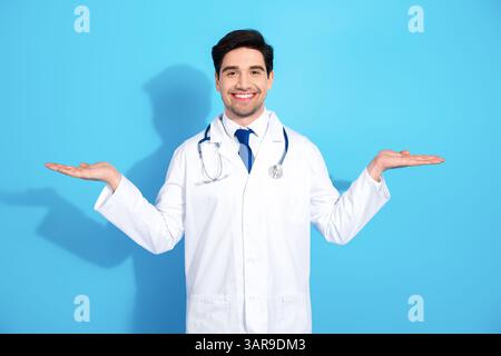Junge Ärztin in weißer Uniform lächelt selbstbewusst vor blauem Hintergrund und betont Professionalität und Gesundheitskonzepte Stockfoto