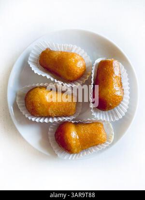 Köstlicher babà Rum, süßer Alkohol Dessert aus gesäuertem Teig, eingeweicht in Rum auf einer weißen Platte. Weißer Holzhintergrund, direkt darüber, Kopierraum. Stockfoto