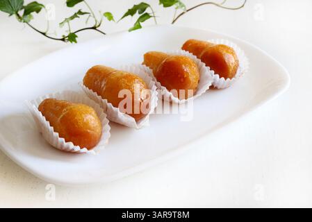Köstlicher babà Rum, süßer Alkohol Dessert aus gesäuertem Teig, eingeweicht in Rum auf einer weißen Platte. Weißer Holzhintergrund, direkt darüber, Kopierraum. Stockfoto