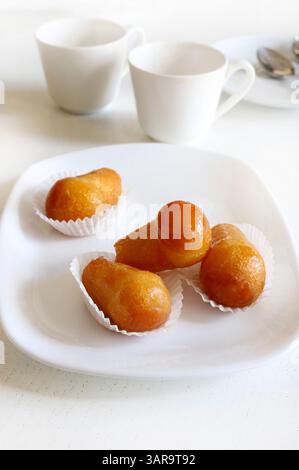 Köstlicher babà Rum, süßer Alkohol Dessert aus gesäuertem Teig, eingeweicht in Rum auf einer weißen Platte. Weißer Holzhintergrund, direkt darüber, Kopierraum. Stockfoto