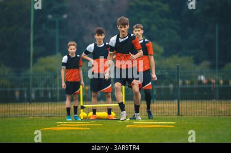 Teenager-Fußballspieler trainieren auf einem Spielfeld und üben Agilitätsübungen mit gelben Körben und Kegeln. Fußball-Sommercamp für Jugendspieler. Teamkollegen in Socc Stockfoto