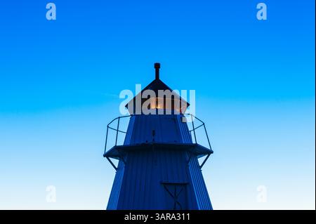 Ein historischer Leuchtturm beleuchtet die Abenddämmerung in Bua, Schweden, eingebettet in ein ruhiges Dorf. Das Leuchtfeuer dient als Leitlicht für vorbeifahrende Boote, Ad Stockfoto