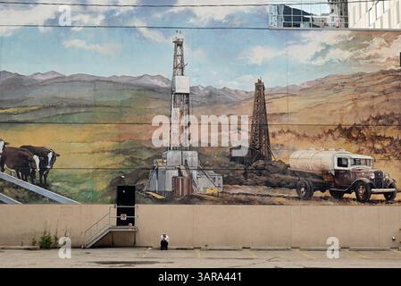 Ein Street Art Gemälde in einer Straße von Calgary erinnert an den Beginn der Ölgeschichte im Bundesstaat Alberta, während eine Frau eine Pause einlegt. Stockfoto