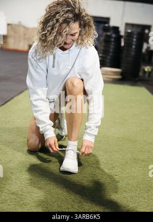 Sportliche Frau, die sich auf das Training vorbereitet, kniend auf dem Fitnessboden Stockfoto