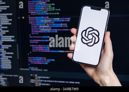 Poznan, Polen – 14. April 2025: Das ChatGPT-Logo wird auf dem Smartphone angezeigt, das vom Entwickler vor dem Code-Editor gehalten wird und die KI-Nutzung in moderner Software veranschaulicht Stockfoto
