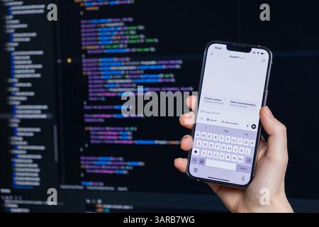 Poznan, Polen – 14. April 2025: Person, die ein Smartphone hält und ChatGPT 4,5-Chat während des Codierens auf einem Computer geöffnet hat, zeigt die Integration von KI-Tools i Stockfoto