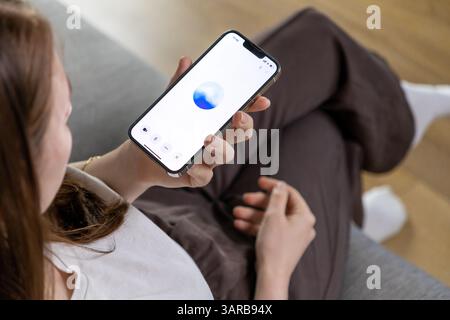 Posen, Polen – 14. April 2025: Eine junge Frau interagiert mit einem Smartphone mit einem GPT-basierten Sprachassistenten und demonstriert moderne KI-Technologie in e Stockfoto