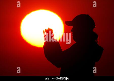Isle Of Palms, Usa. April 2025. Ein Fotograf mit der Silhouette des Sonnenaufgangs macht Fotos, während die Sonne am Strand des Wild Dunes Resort am 17. April 2025 in Isle of Palms, South Carolina, über den Horizont steigt. Quelle: Richard Ellis/Richard Ellis/Alamy Live News Stockfoto